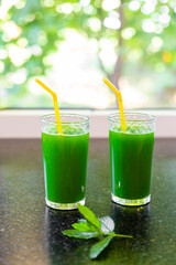 A green drink made from fresh vegetable greens with chlorophyll in glasses on the countertop, against the background of the window