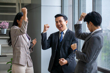 Asian business team celebrate corporate victory together in office, laughing and rejoicing, smiling excited employees colleagues screaming with joy in office.