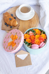 Cup of coffee,croissant,blueberries on wooden tray.Romantic breakfast in bed with box of orange roses,macarons,envelope with note.Birthday,Valentine's day morning. Honeymoon concept.Delivery service