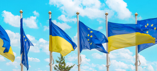 Ukraine and European Union flags on poles fluttering by wind on blue sky. Ukrainian flag panorama