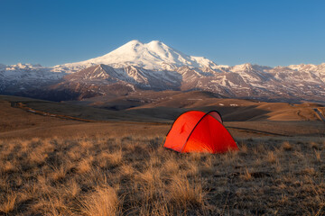Golden light sunrise with bright red tent in front of snow-covered Mount Elbrus, Caucasus, Russia
