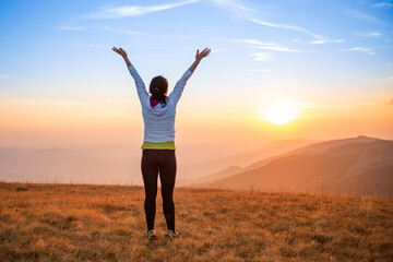 Fototapeta na wymiar Young happy woman jumping at sunset mountains with sunset hills and mountain landscape