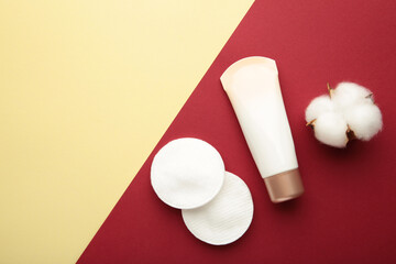 Cream package with cotton pads and flower on red and beige background. Beauty skincare products.