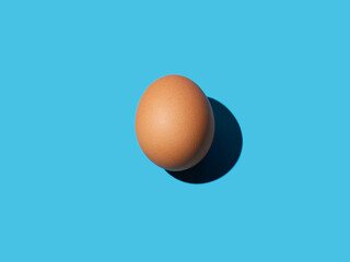 A brown chicken egg lies in the center on a bright blue background. Bright light, deep shadow. Close-up, copy space, top view.