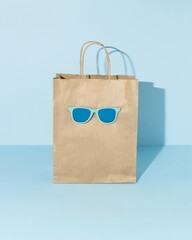 Paper bag with sunglasses and empty space on it. Blue background. Shopping concept.