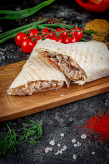 Shawarma with vegetables on a wooden board with pita sauce on a dark stone table decorated with cherry tomatoes. Fast food restaurant, delivery service.