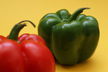 Big green pepper with blurred red pepper on orange background. Shallow depth of field