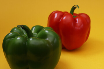 Big green pepper with blurred red pepper on orange background. Shallow depth of field