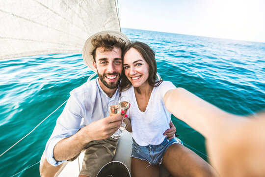 Happy couple of lovers enjoying sail boat trip experience in the ocean - Boyfriend and girlfriend taking selfie picture outside on summer vacation