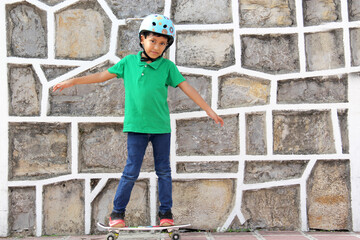 Little dark-haired Latino boy plays in the park with his skateboard wearing a helmet 