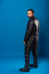 portrait of a man in a studio in a black leather coat. model with a beard on a blue background.