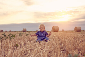 Naklejka na ściany i meble Happy little girl in the wheat field. girl smiling and happy. Nature in the country