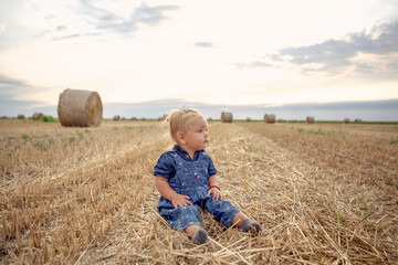 Naklejka na ściany i meble baby girl with a beautiful smile at gold wheat field.