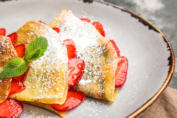 Plate of thin pancakes with strawberries, sugar powder and mint leaves on dark background, closeup