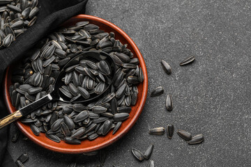 Bowl, spoon and napkin with black sunflower seeds on dark background