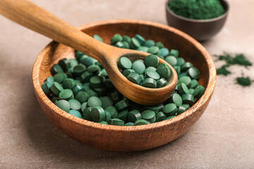 Bowl of spirulina pills with spoon on beige background, closeup