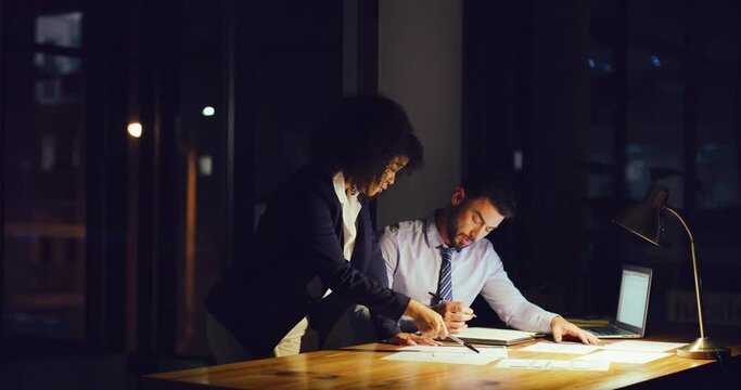 Two businesspeople having a discussion while working late in an office. Female leader or mentor giving instructions or ideas on paperwork with colleague at night. Accountants trying to reach deadline