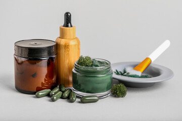 Composition with jar of spirulina facial mask, pills and cosmetics on light background
