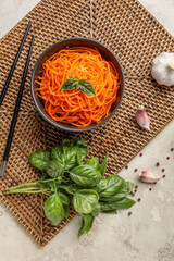 Composition with bowl of tasty korean carrot salad, spices and basil on light background