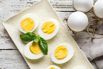 Plate with halves of boiled chicken eggs on light wooden background, closeup