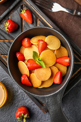 Frying pan with mini pancakes and strawberry on dark background