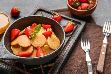 Wooden board with frying pan of mini pancakes and strawberry on table