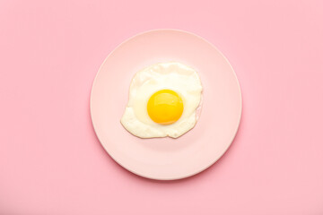 Plate with fried egg on pink background