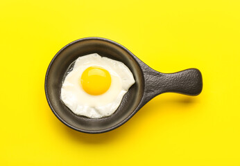 Frying pan with tasty egg on yellow background