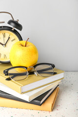 School books with apple, eyeglasses and alarm clock on table against grey background