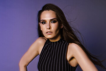 Naklejka premium Fashion portrait of a brunette with long hair and 90s style makeup through a crystal filter, overalls and a red leather belt on a purple background