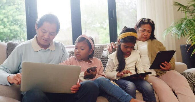 Asian Children And Grandparents Addicted To Modern Technology While Sitting On Sofa. Multi Generation Family Using Wireless Devices While Bonding. Kids Teaching Grandfather How To Use Internet