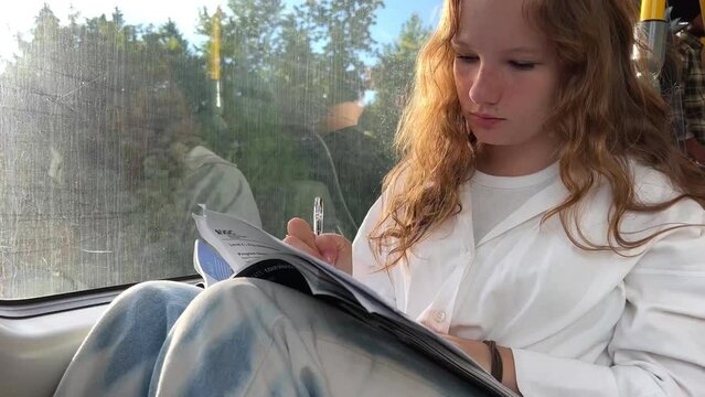 European girl in a white shirt rides in skytrain a teenage girl does her homework to hold a notebook on her knees she gets home from Vancouver Surrey nature flickers through the window and goes home