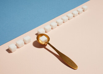 One cube sugar in spoon and many sugar cubes on blue and pink background. Concept flat lay, view from the top.