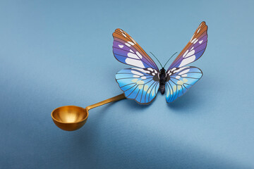Blue butterfly siting on golden spoon and kipping balance on blue background. © Naz