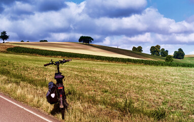 Bicycle parked at the edge of a meadow in front of a wheat field in the hilly landscape of Saxony, bicycle tour through Saxony