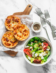 Delicious lunch table - mini canned tuna, mozzarella quiche and fresh greek salad on a light background, top view
