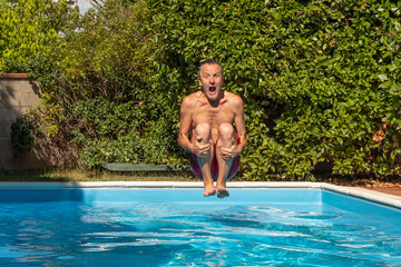 A middle-aged white man dives into a pool, cannonball style, with a funny expression - obrazy, fototapety, plakaty