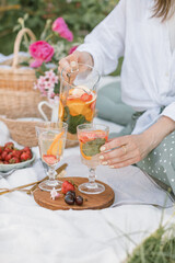 Close up of girl pouring lemonade into glasses at a summer picnic. Beautiful plastic free picnic outdoors.