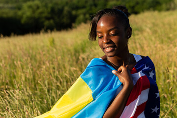 African american woman wrapped in american and ukrainian flag flutters waving in the wind. Stand...