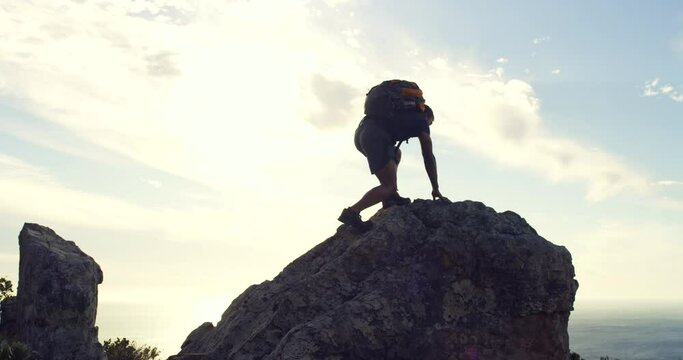 Man reaching the top of a mountain against sunset sky background with copyspace. Young fit mans fitness goals, celebrating successfully climbing a mountain and lifting his arms in a winning gesture