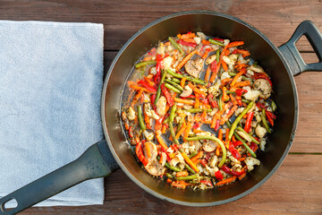 Frying pan with stewed vegetables top view on a wooden table. Horizontal photo