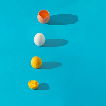 Colorful pattern made of raw cracked egg, boild eggwhite and yolk on blue background with long shadow.  Square composition with copy space.