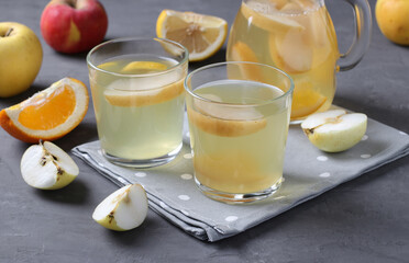 Compote of oranges, apples and lemon in two glasses and jug on dark gray background