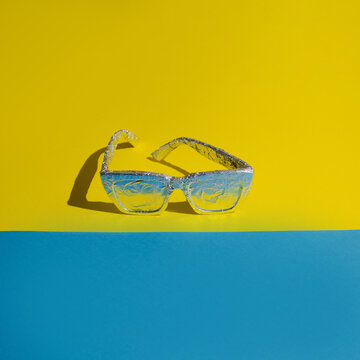 Concept Made With Sunglasses Wrapped In Aluminum Foil On A Blue And Yellow Background. The Idea Of ​​maximum Sun Protection And Insulation.