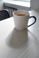 White cup with hot tea on a light wooden background. Place for text
