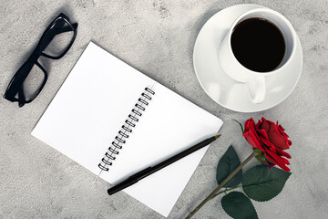 Notebook with coffee, pen, reading glasses, roses on white marble table.