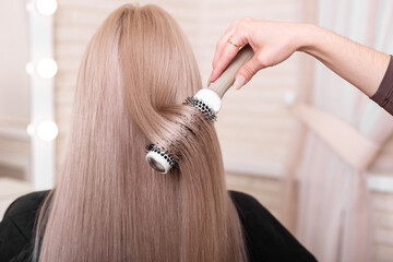 Fototapeta premium Hairdresser's hand brushing long silver blonde hair in beauty salon