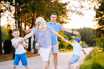 Two naughty boys pulls their mother by the hands, wanting to stay at park. The capricious children resists and does not want to leave. Upset confused father spreading his arms stand behind