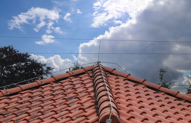 A roof with red shingles and a lightning conductor on it. - obrazy, fototapety, plakaty