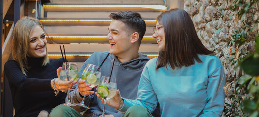 Happy friends sitting on stairs  and celebrating their long-awaited gathering with soft drinks, portrait shot